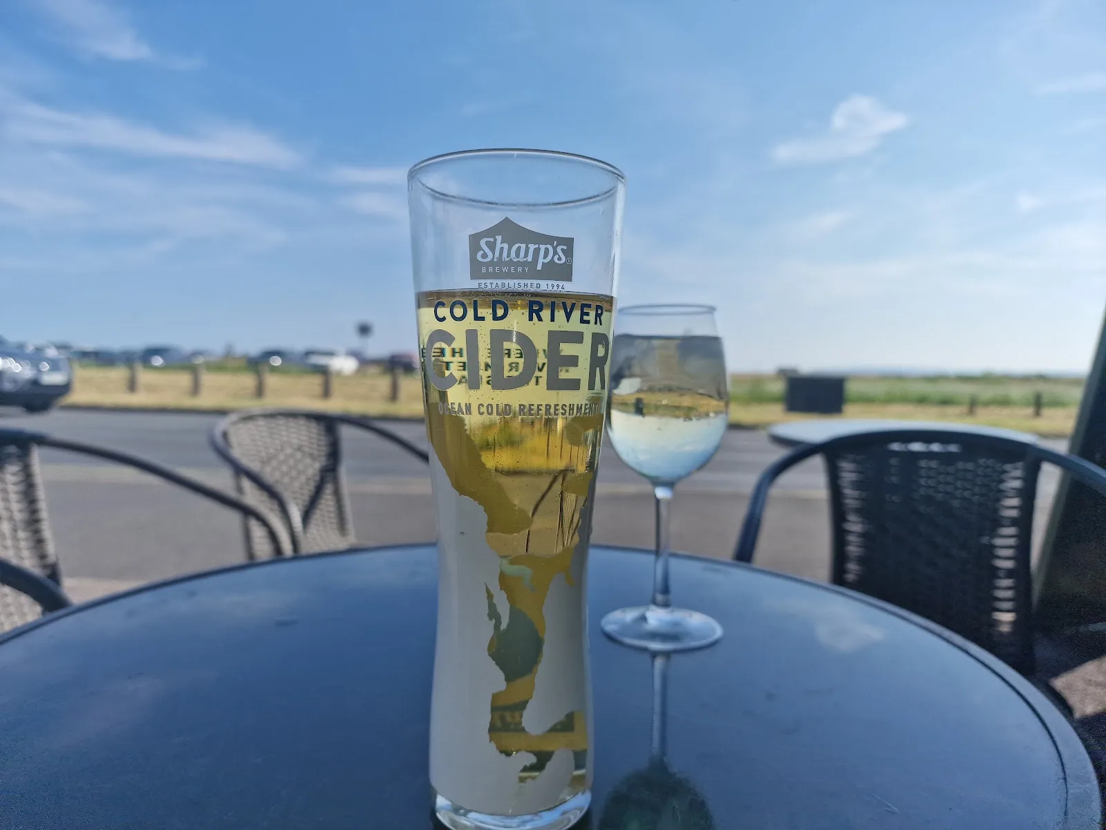 A pint of cider and a glass of white wine on an outside table at The Olive Leaf, looking towards the seafront
