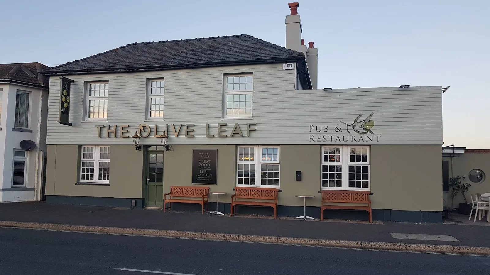 The front of The Olive Leaf at dusk, with benches and lanterns by the door